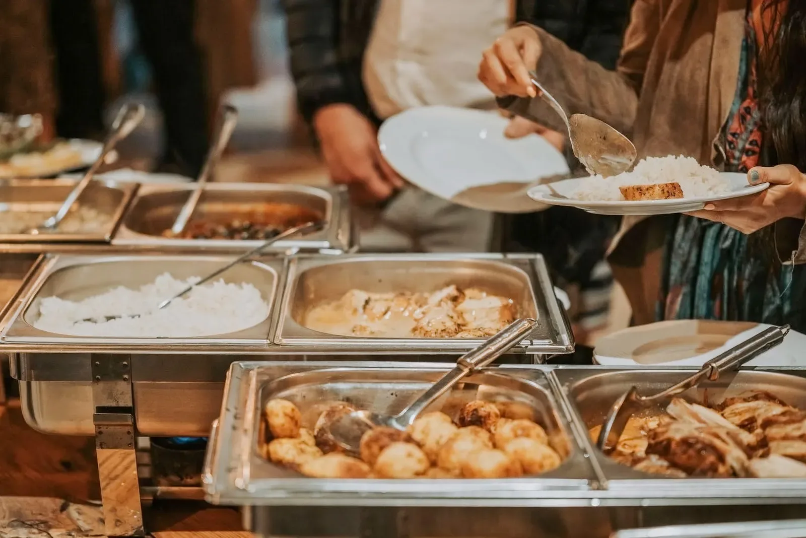 Hosszú, elegánsan megterített finger food büféasztal egy rendezvénytéren, állóasztalokkal és a háttérben dolgozó munkatársakkal